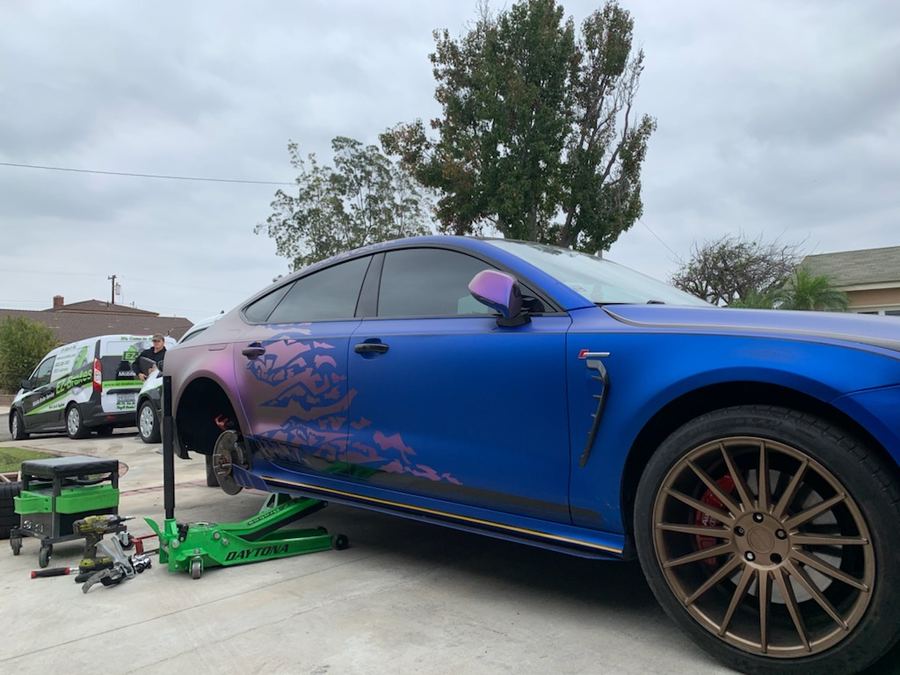 Blue sports sedan raised for mobile brake service with the EZ-Brakes van nearby