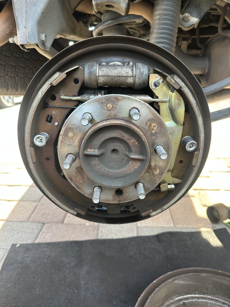 Rear brake drum backing plate and wheel cylinder exposed during a mobile brake shoe replacement
