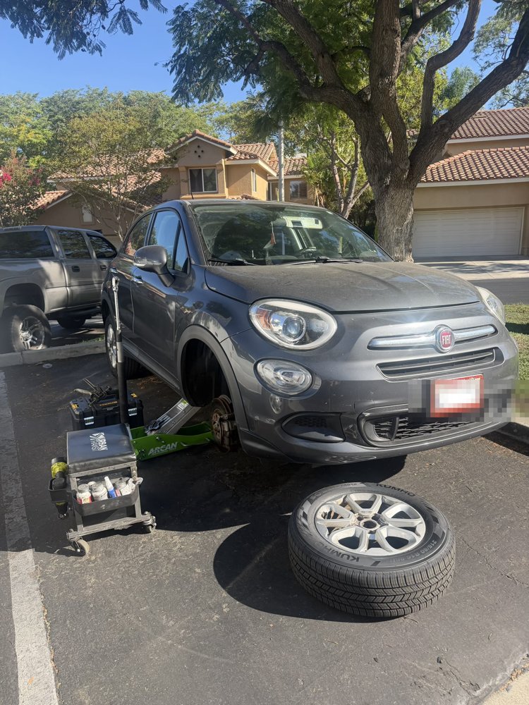 Gray Fiat 500X raised on a jack during mobile brake service in a Rancho Santa Margarita driveway