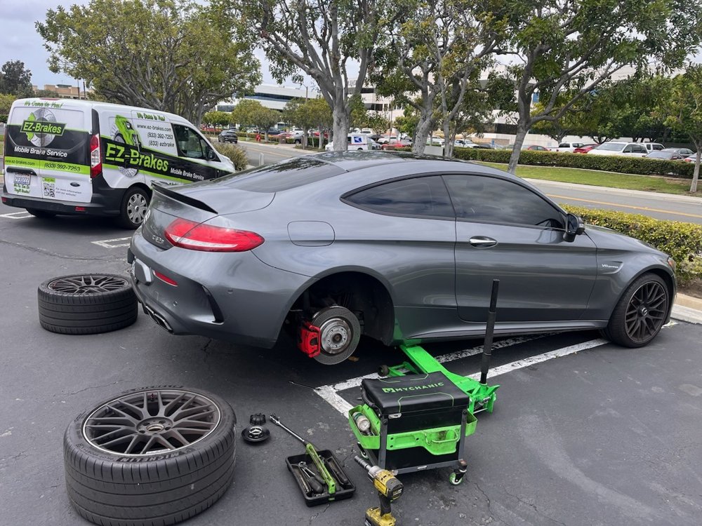Gray Mercedes-AMG C63 with rear wheel removed during mobile brake service in an Anaheim parking lot, EZ-Brakes van parked alongside