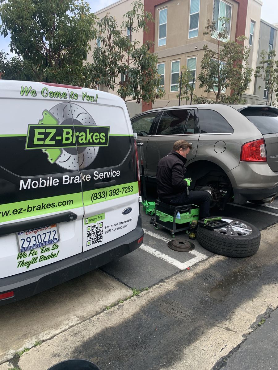 Mobile brake technician servicing a silver sedan in a driveway