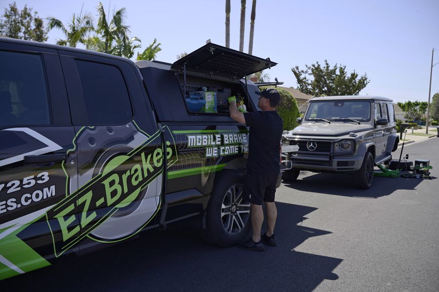 Mobile brake technician servicing a vehicle with EZ-Brakes trucks parked nearby