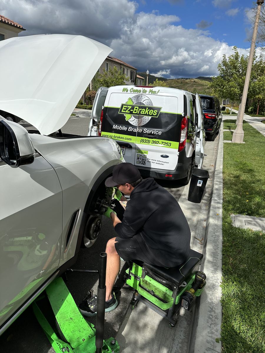 Mobile brake technician servicing an SUV curbside with the EZ-Brakes van nearby
