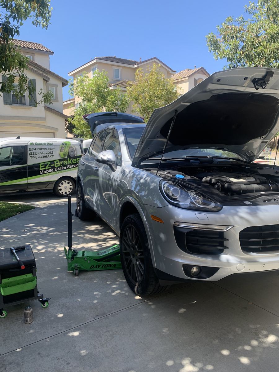 Mobile brake technician working under a white Jeep Grand Cherokee