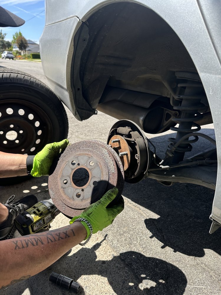 EZ-Brakes technician holding a worn brake drum during a mobile brake drum replacement
