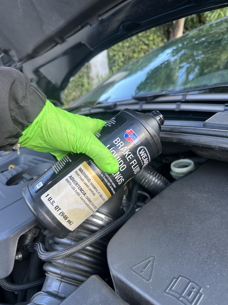 EZ-Brakes technician in green gloves pouring fresh brake fluid into the reservoir during a mobile brake fluid flush