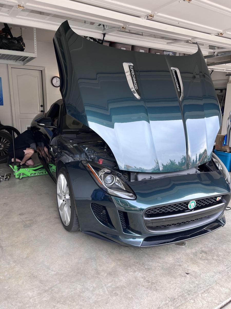 Technician servicing a dark Jaguar F-Type in a home garage
