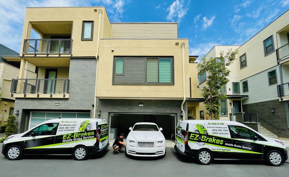 Two EZ-Brakes mobile service vans parked outside a residential job, flanking a customer's vehicle
