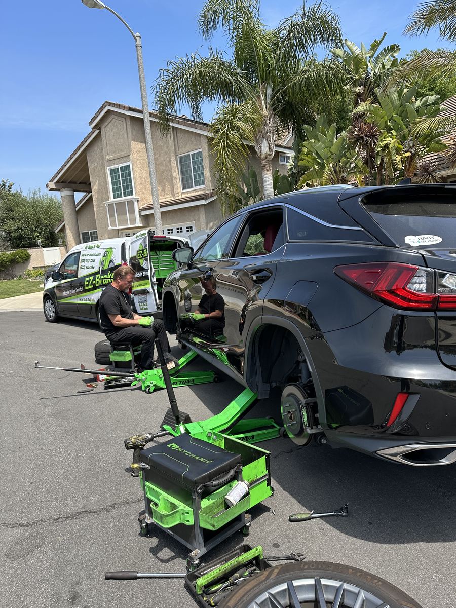 Two EZ-Brakes technicians servicing a black Lexus RX in a driveway