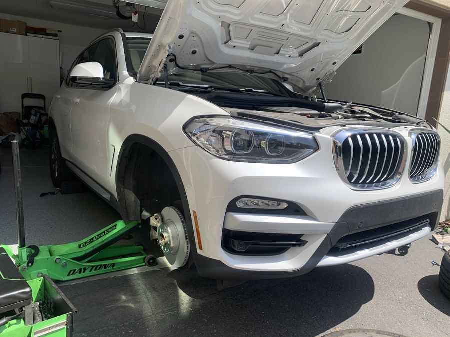White BMW X3 raised for mobile brake service in a home garage