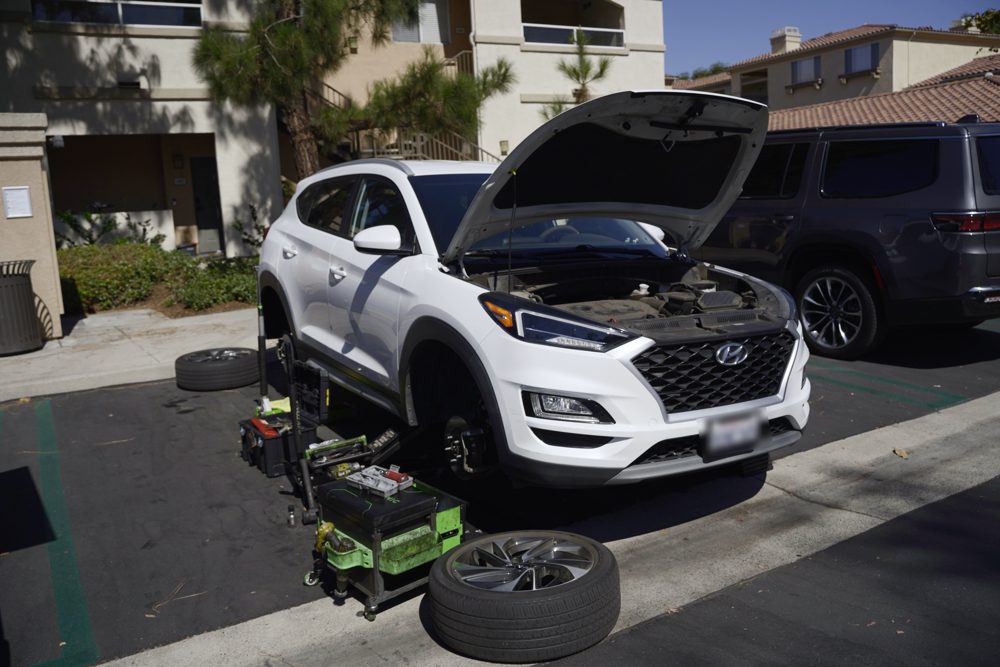 White Hyundai Tucson with front wheel removed during mobile brake service in an Irvine apartment complex parking lot