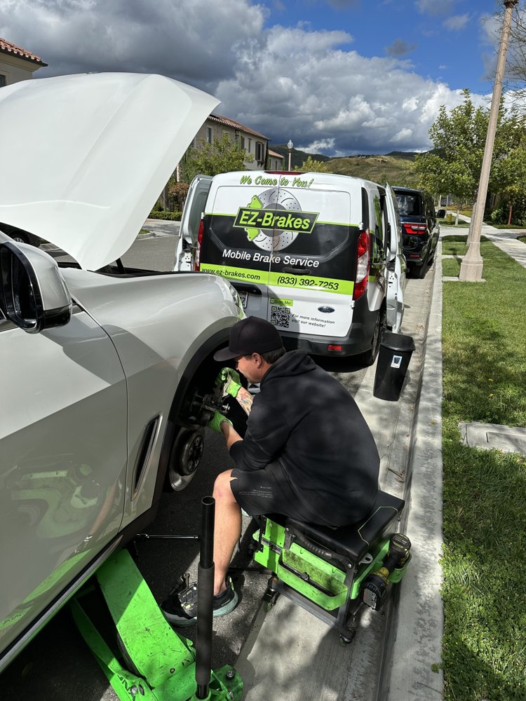 EZ-Brakes technician working on a white SUV's front brakes curbside in Ladera Ranch